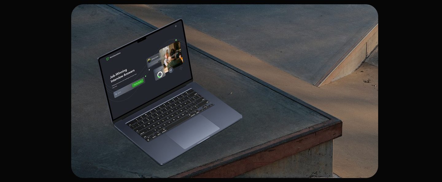 Laptop on a concrete ledge displaying the MockQuestions homepage hero, its dark screen showing the Job-Winning Interview Answers headline, search bar, and green button.
